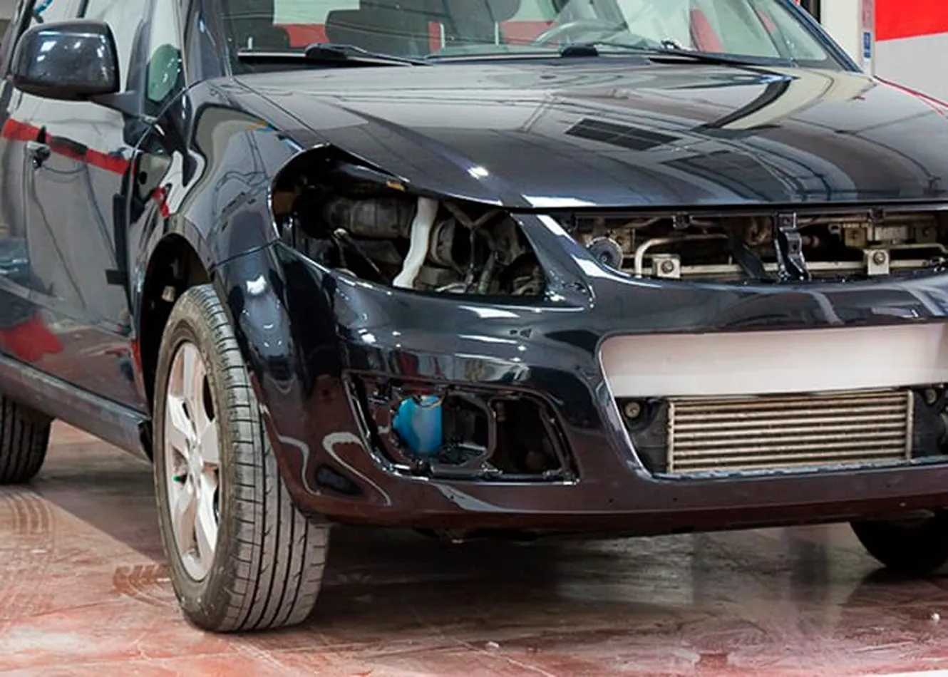Proceso de reparación frontal en taller especializado Reparación frontal de coche negro tras desmontaje de piezas